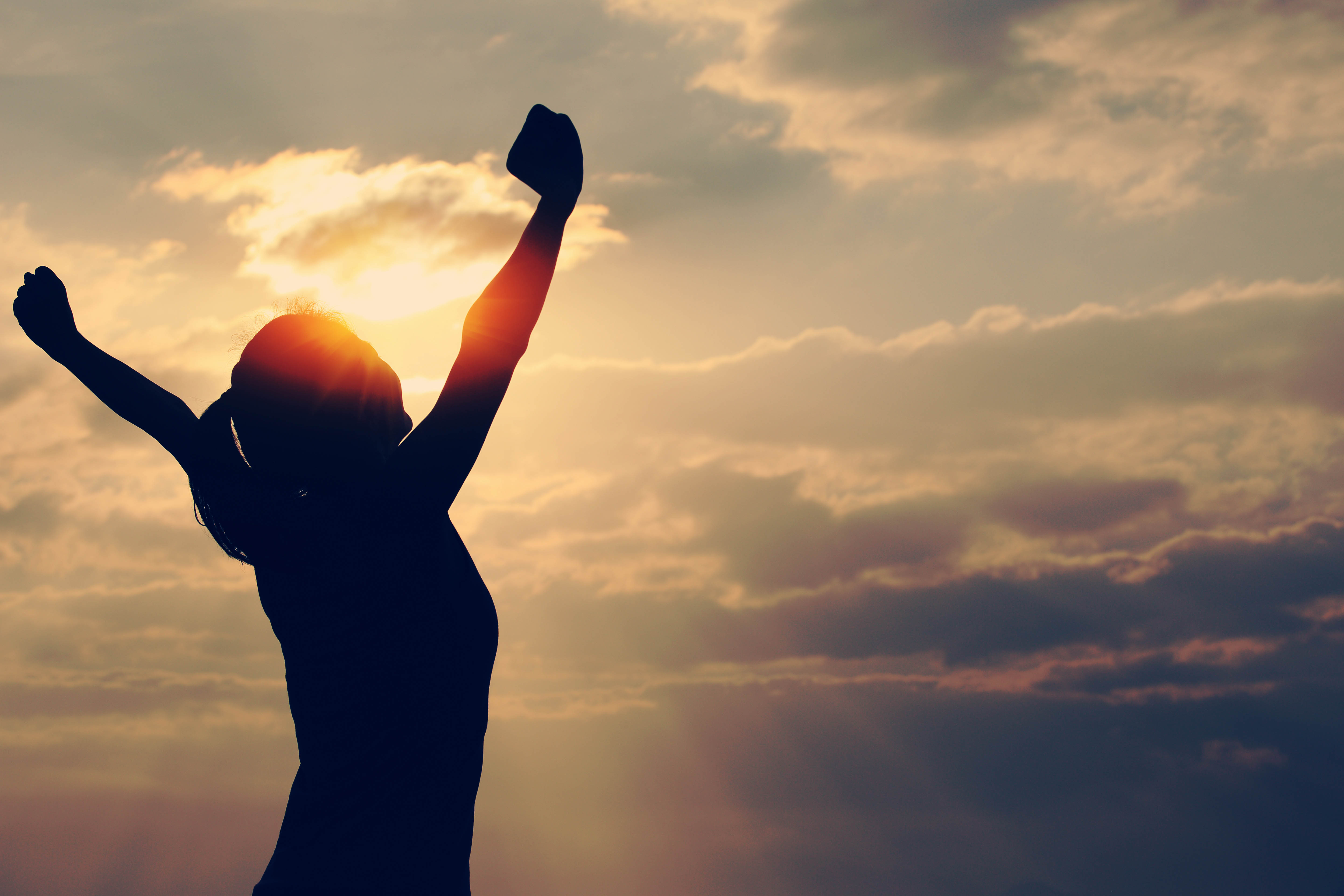 Silhouette of woman celebrating on the beach in the sunrise